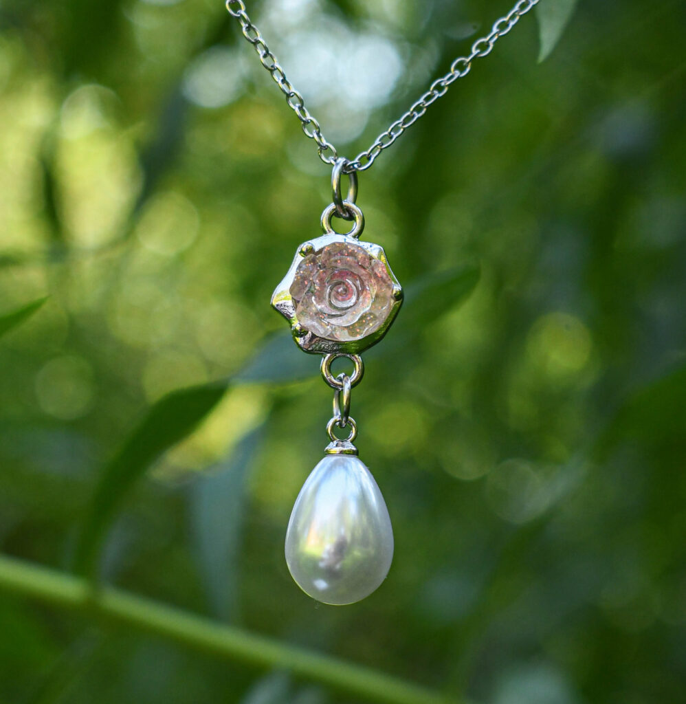 Roosa läikiva roosiõie ja pärliga kaelakee esi