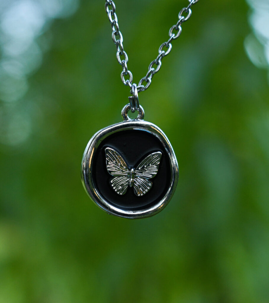 Liblikas mustal taustal ümmarguses ripatsis