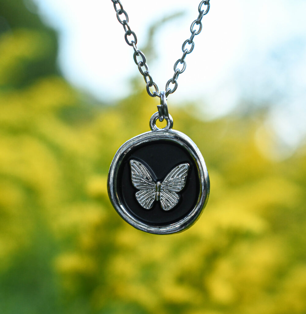 Liblikas mustal taustal ümmarguses ripatsis