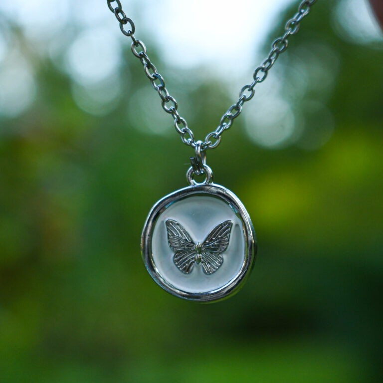 Liblikas valgel taustal ümmarguses ripatsis