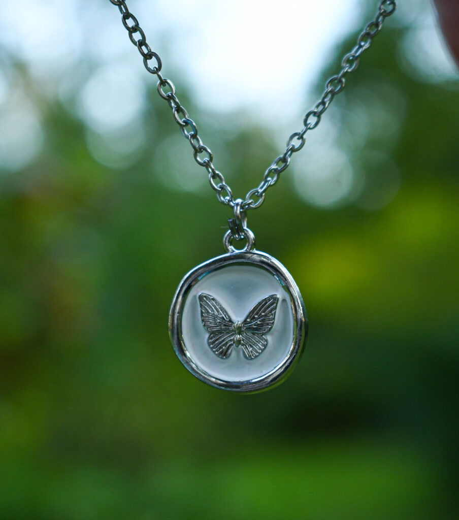 Liblikas valgel taustal ümmarguses ripatsis