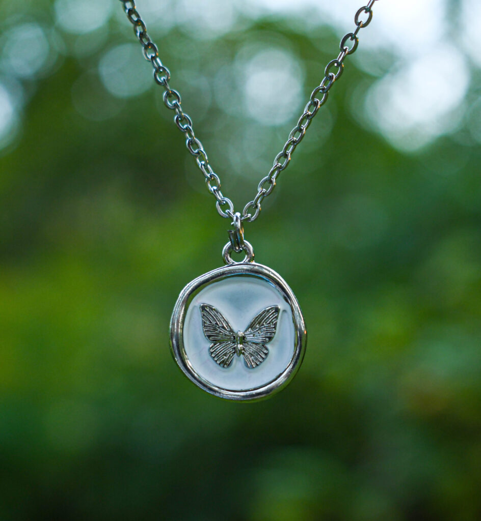 Liblikas valgel taustal ümmarguses ripatsis