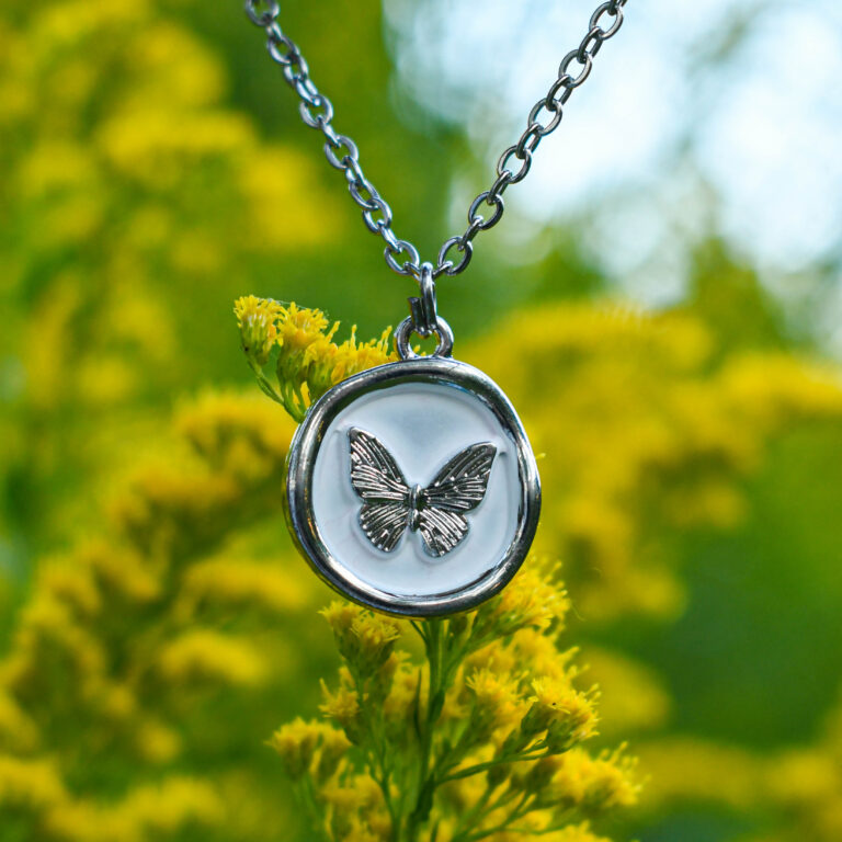 Liblikas valgel taustal ümmarguses ripatsis