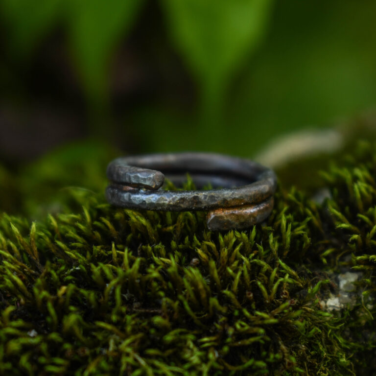Puhtast vasest spiraalkujuline sõrmus samblal, tumeda patina ja soojade vasksete detailidega.